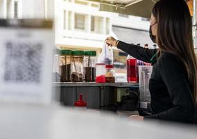 eine Seitenansicht einer Verkäuferin, die eine Tasse Kaffee durch ein Glas reicht. foto