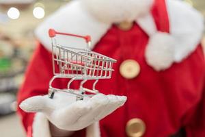 der weihnachtsmann, der im supermarkt einkauft, zeigt einen mini-wagen, ein weihnachts- und einkaufskonzept. foto