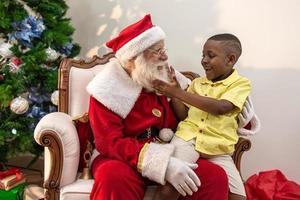 weihnachtsmann liefert einem kleinen afrikanischen jungen eine geschenkbox. Heiligabend, Lieferung von Geschenken. foto