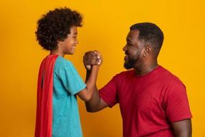 Afrikanischer Vater und Sohn spielen tagsüber Superhelden. Leute, die Spaß am gelben Hintergrund haben. Konzept der freundlichen Familie. foto