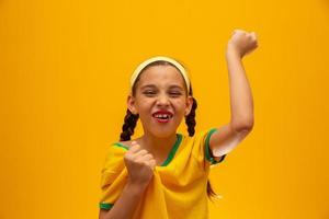 Fußballfan, brasilianische Mannschaft. Weltmeisterschaft. Schönes kleines Mädchen, das ihr Team auf gelbem Hintergrund anfeuert foto