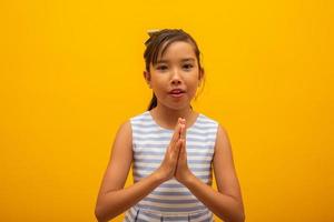 kleines Mädchen, das auf gelbem Hintergrund betet. Kleines asiatisches Mädchen betet mit der Hand, Hände gefaltet im Gebetskonzept für Glauben, Spiritualität und Religion. foto