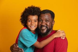 Afrikanischer Vater und Sohn spielen tagsüber Superhelden. Leute, die Spaß am gelben Hintergrund haben. Konzept der freundlichen Familie. foto