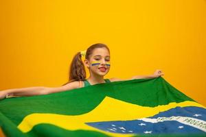 Fußballfan, brasilianische Mannschaft. Weltmeisterschaft. Schönes kleines Mädchen, das ihr Team auf gelbem Hintergrund anfeuert foto