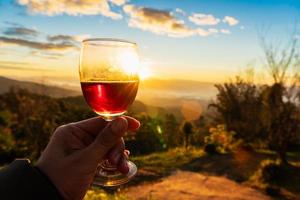 Die Hand des Mannes, die ein Glas Wein auf dem Hintergrund des Sonnenuntergangs hält. foto