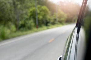 abstrakt und verschwommen neben dem Auto auf der Straße. Blick von neben nach hinten Auto kann Unschärfe von Fensterglas sehen. und verschwommen vom autofahren auf asphaltstraße mit grünem gras und bäumen. Reise in die Natur. foto