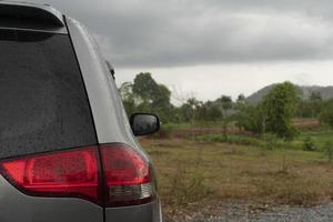 Rückseite des grauen Autostopps oder Parken auf der Karosserie mit Regentropfen. mit Hintergrund von grünem Gras und Bäumen im Garten. Reisen in die Naturgebiete der Provinzen. Feuchtigkeit nach Regen. foto