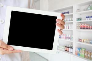 Apothekerin mit Tablet-PC gegen Nahaufnahme von Medikamentenregalen foto