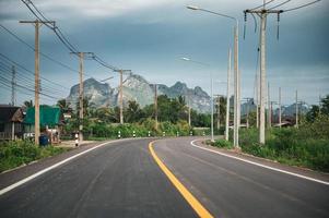 Asphaltstraße mit Bergkette und Strommast und Laternenpfahl auf dem Land bei Sam Roi Yot