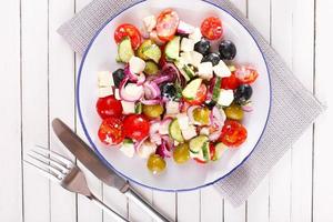 Griechischer Salat serviert in Teller auf Serviette auf hölzernem Hintergrund