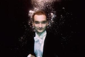 Porträt des jungen Mannes in Fliege und Frack unter Wasser auf dem schwarzen Hintergrund foto