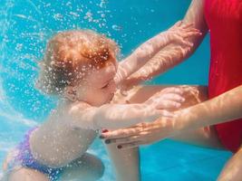 lächelndes kleines Mädchen, das unter Wasser blaues Becken taucht. aktiver lebensstil, kinderschwimmunterricht mit den eltern. Wassersportaktivitäten während der Sommerferien der Familie im tropischen Resort foto