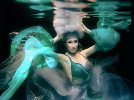 Kunstporträt der jungen schönen Frau im grünen Kleid auf schwarzem Hintergrund unter Wasser im Schwimmbad foto
