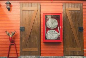 Feuerwehrschlauch im roten Schrank, der an der orangefarbenen Holzwand hängt. Feuernotausrüstungskasten für Sicherheits- und Sicherheitssystem. Feuer Sicherheitspumpe. Sintflutsystem des Feuerlöschsystems. Sanitär Brandschutz.