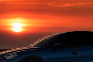 blaues kompaktes suv-auto mit sport und modernem design, das abends bei sonnenuntergang auf einer betonstraße am meer geparkt ist. hybrid- und elektroauto-technologiekonzept. Pkw-Stellplatz. Automobilindustrie. foto