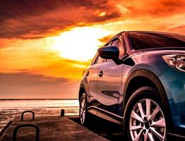 blaues luxus-suv-auto geparkt auf betonstraße am meeresstrand mit schönem roten sonnenuntergangshimmel. sommerferien am tropischen strand. Ausflug. Vorderansicht Sport und modernes Design-SUV-Auto. Sommerreise mit dem Auto. foto