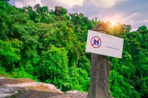 Gehen Sie nicht vom Weg ab. Warnzeichen im Nationalpark hängen an Betonpfosten am Wasserfall im grünen Tropenwald. warnschild für reisende, um unfälle während der spur zu verhindern. Zeichen für Sicherheit. foto