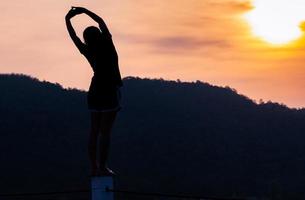 gesunde frau, die morgens arme und körper streckt, mit schönem sonnenaufgang über dem berg. glückliche junge weibliche Übung im Park. Outdoor-Workout vor dem Fitnesstraining. aktive frau aufwärmen. foto