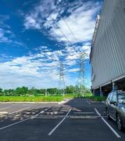 PKW-Stellplatz im Einkaufszentrum für den Kundenservice. Asphalt-Parkplatz im Freien an sonnigen Tagen mit grünem Baumwald und Hochspannungsturm. Oberleitung. foto