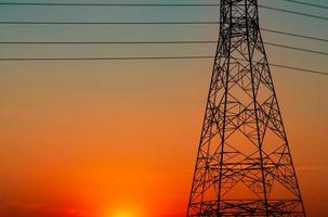 Silhouette Hochspannungsmast und Elektrokabel mit einem orangefarbenen Himmel. Strommasten bei Sonnenuntergang. Kraft- und Energiekonzept. Hochspannungsnetzturm mit Drahtkabel an der Verteilerstation. foto