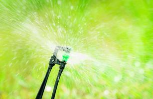 Nahaufnahmesprinkler, der Gras auf grünem Hintergrund der Unschärfe bewässert. Regner mit automatischem System. gartenbewässerungssystem bewässerung rasen. Sprinkler Wartungsdienst. Bewässerungssprinkler für den Heimgebrauch. foto