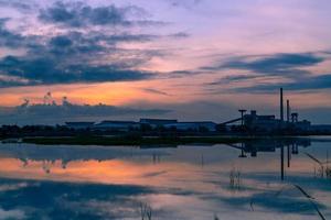 Landschaft von Fabrikgebäuden mit dunkelblauem und orangefarbenem Sonnenuntergang über dem Wasser im Fluss. Lagerhalle bei Nacht. saubere Umgebung rund um die Fabrik. Fabrik geschlossen. foto