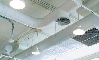 Luftkanal, Klimaanlagenrohr und Sprinkleranlage an weißer Deckenwand. Luftstrom und Belüftungssystem. Gebäudeinneres. Deckenleuchte mit offenem Licht. Konzept der Innenarchitektur. foto