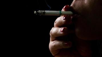 Frau mit rotem Nagel raucht Zigarette auf dunklem Hintergrund. konzept mit dem rauchen aufgeben. Eine schlechte Angewohnheit bei Frauen kann zu Alterung und Lungenkrebs führen. gestresste Frau. nikotinsüchtig. 31 mai weltnichtrauchertag.
