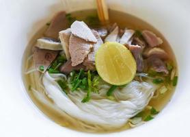 köstliche nudelschüssel - vermicelli-nudelsuppe würzig mit schweinefleischeintopf gemüse und zitrone in der schüssel traditionelles thailändisches und chinesisches essen aus asien, schweineinnereien, leberschweinedarm foto