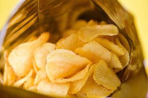 Kartoffelchips sind Snacks in Beutelverpackungen, die in Plastik verpackt sind, fertig zum Verzehr und fetthaltige Lebensmittel oder Junk Food, Kartoffelchips auf gelbem Hintergrund foto
