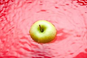 schwimmender apfel auf rotem hintergrund. Wasseroberfläche mit einem schwimmenden grünen Apfel. foto