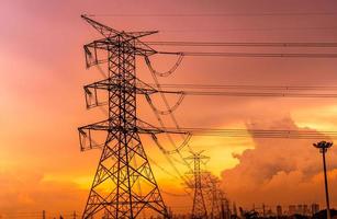 elektrische hochspannungsmasten und übertragungsleitungen mit orangefarbenem sonnenunterganghimmel und modernem bürogebäudehintergrund des stadtbildes. Strommasten. Kraft und Energie für die Stadt. Hochspannungsnetz Turm. foto