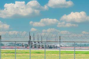 Metallzaun des Flughafens und unscharfes Flugzeug, das auf dem Parkplatz des Flughafens geparkt ist. Viele geparkte Flugzeuge und Flüge sind von einem Coronavirus betroffen. Krise im Luftfahrtgeschäft. Zaun gegen den blauen Himmel. foto