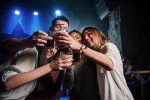 stellen Sie Ihre Getränke auf. Gruppe junger Freunde, die im Nachtclub lächeln und anstoßen foto