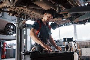 auf der Suche nach benötigten Instrumenten. mann in der werkstatt in uniform repariert defekte teile des modernen autos foto