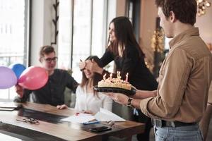 Kerl hält Kuchen für das Mädchen. einer der mitarbeiter hat heute geburtstag. freundliche Mitarbeiter beschließen, sie zu überraschen foto