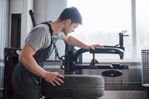 Einsetzen des Elements in den Reifen. junger mann arbeitet tagsüber mit radscheiben in der werkstatt foto