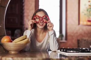 mit Pfefferringen spielen. hübsche junge frau, die in der modernen küche nahe gasherd steht foto