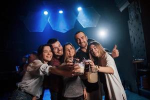 Brille klopfen. Gruppe junger Freunde, die im Nachtclub lächeln und anstoßen foto