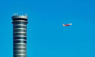 Flugsicherungsturm auf dem Flughafen mit internationalem Flugflugzeug, das am klaren blauen Himmel fliegt. Verkehrskontrollturm für Flughäfen zur Kontrolle des Luftraums durch Radar. Luftfahrttechnik. Flugmanagement. foto