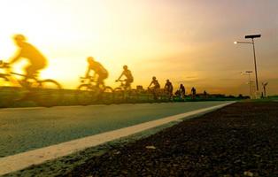 verwischen Sie Fotosportler fahren Fahrräder mit Geschwindigkeitsbewegung auf der Straße am Abend mit Sonnenunterganghimmel. Sommerübungen im Freien für ein gesundes und glückliches Leben. radfahrer, der mountainbike auf radweg fährt. Team. foto