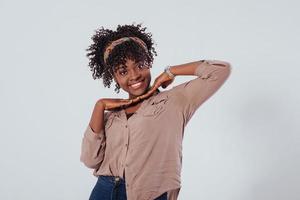 Fröhliche Frau hält ihre Hände vor den Hals. Schönes afroamerikanisches Mädchen mit lockigem Haar im Studio mit weißem Hintergrund foto