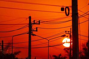 Strommast und Hochspannungsleitungen am Abend. Strommasten mit Drahtseil und Straßenlaterne bei Sonnenuntergang. Macht und Energie in der ländlichen Stadt. schöner roter sonnenunterganghimmel hinter strommasten. foto