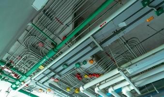 elektrisches Leitungssystem und verzinktes Stahlrohr mit elektrischem Kabel, das an der Decke installiert ist. pvc-kunststoffrohr des entwässerungssystems und sauberes wasser an der decke des industriegebäudes. Bauen & Konstruktion. foto