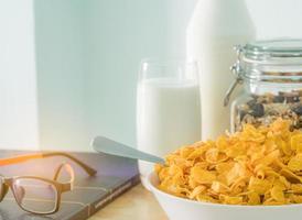 Müslischale mit Löffel und ein Glas Milch auf Holztisch in der Nähe von Diabetes-Lehrbuch und Brille. Calcium-Lebensmittel-Frühstück. Cornflakes und Milchkonzept foto
