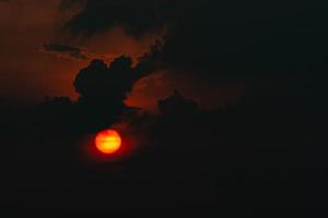 rote große sonne in dunklen wolken. Teufel Sonnenuntergang. Horrorblick auf die Sonne im schwarzen Wolkenhimmel. Sommer Sonnenuntergang. feurige sonne am abend. Naturhintergrund. Dramatischer Himmel mit großer Sonne. heißes Wetter. Himmelskonzept. foto