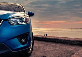 blaues kompaktes suv-auto mit sport und modernem design, das abends bei sonnenuntergang auf einer betonstraße am meer geparkt ist. hybrid- und elektroauto-technologiekonzept. Pkw-Stellplatz. Automobilindustrie. foto