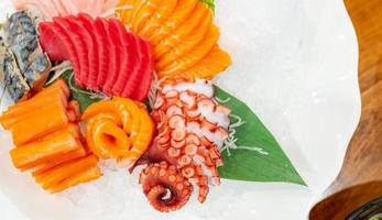 Combo-Set für japanisches Essen. Lachs, Thunfisch-Sashimi, Riesenkrake und Krabbenstäbchen werden mit Crushed Ice in einer weißen Platte auf dem Restauranttisch serviert. Fischfleisch geschnitten. Buffet mit Meeresfrüchten. Gesundes japanisches Essen. foto