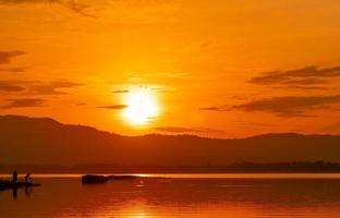 schöner sonnenaufgangshimmel über dem berg am reservoir. Leute fischen mit einer Angelrute auf dem Fluss. Landschaft aus Stausee und Berg mit orangefarbenem Sonnenaufgangshimmel. Silhouettenleben am Morgen. foto