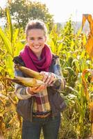 glückliche junge Frau, die Mais beim Stehen im Maisfeld hält